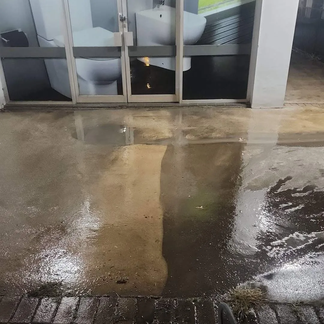 Concrete outside a shopfront part way through cleaning, the washed strip pale against the soiled slab around it.