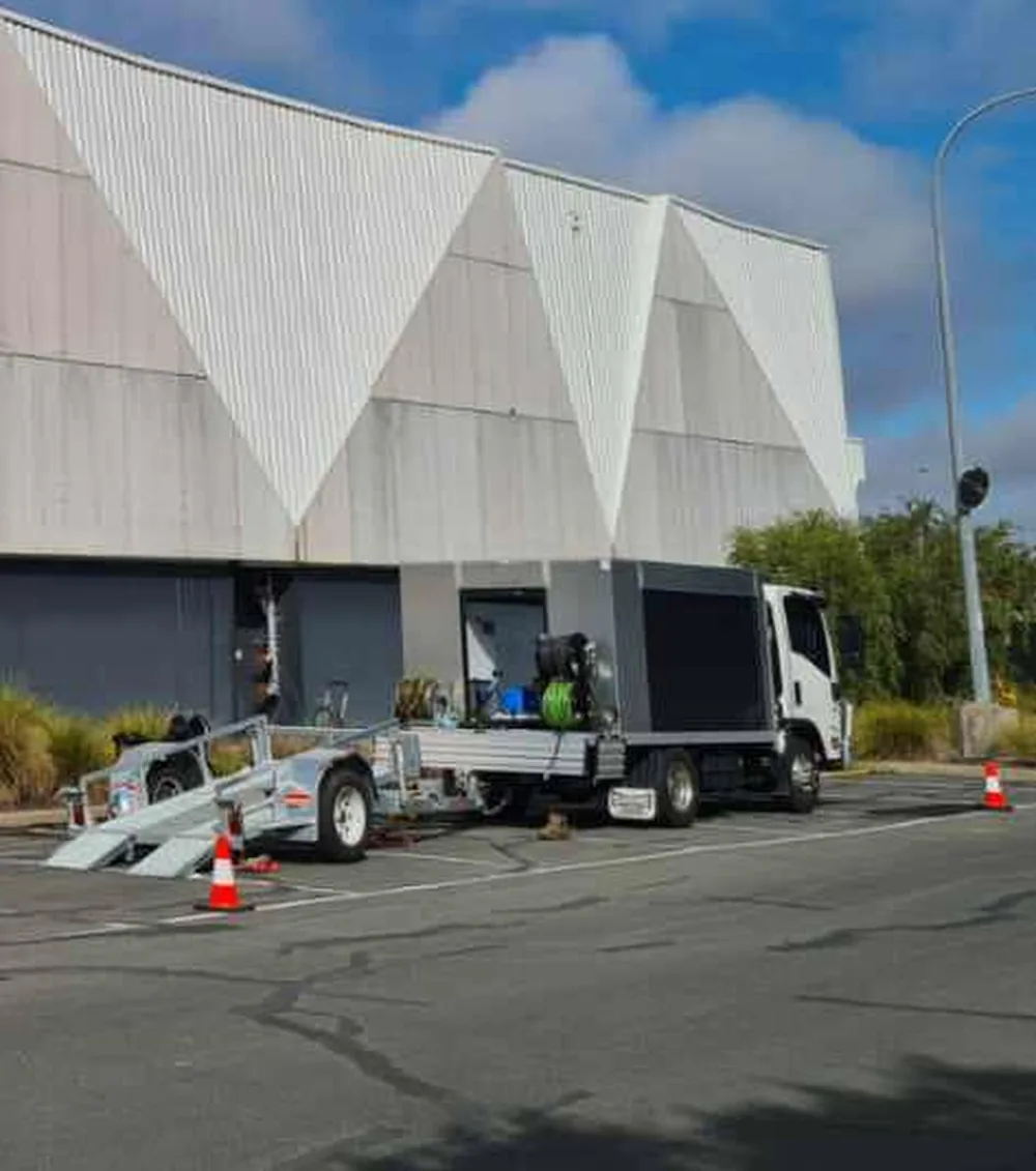 The truck and plant trailer set up in a commercial car park, traffic cones out and the hose reel visible in the open side of the truck body.